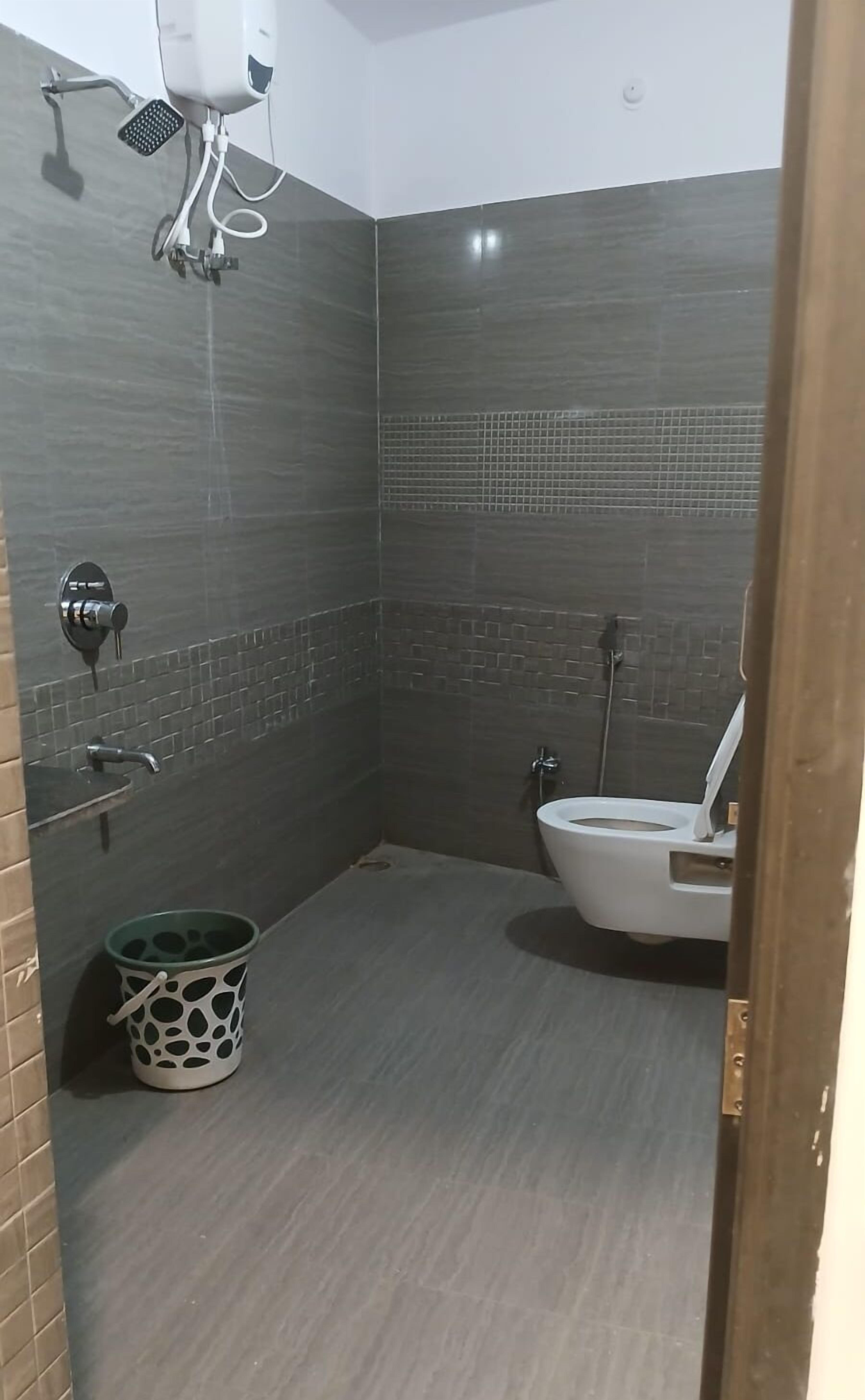 Ein kleines, modernes Badezimmer mit dunklen Fliesen, einer Duschbrause, einer Toilette und einem Eimer.