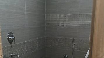 Ein kleines, modernes Badezimmer mit dunklen Fliesen, einer Duschbrause, einer Toilette und einem Eimer.