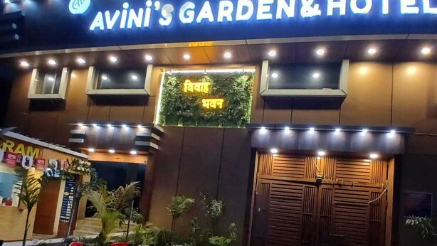Jardines y Hotel Avini, con una entrada bien iluminada, una zona de recepción y un pequeño espacio al aire libre con sillas.