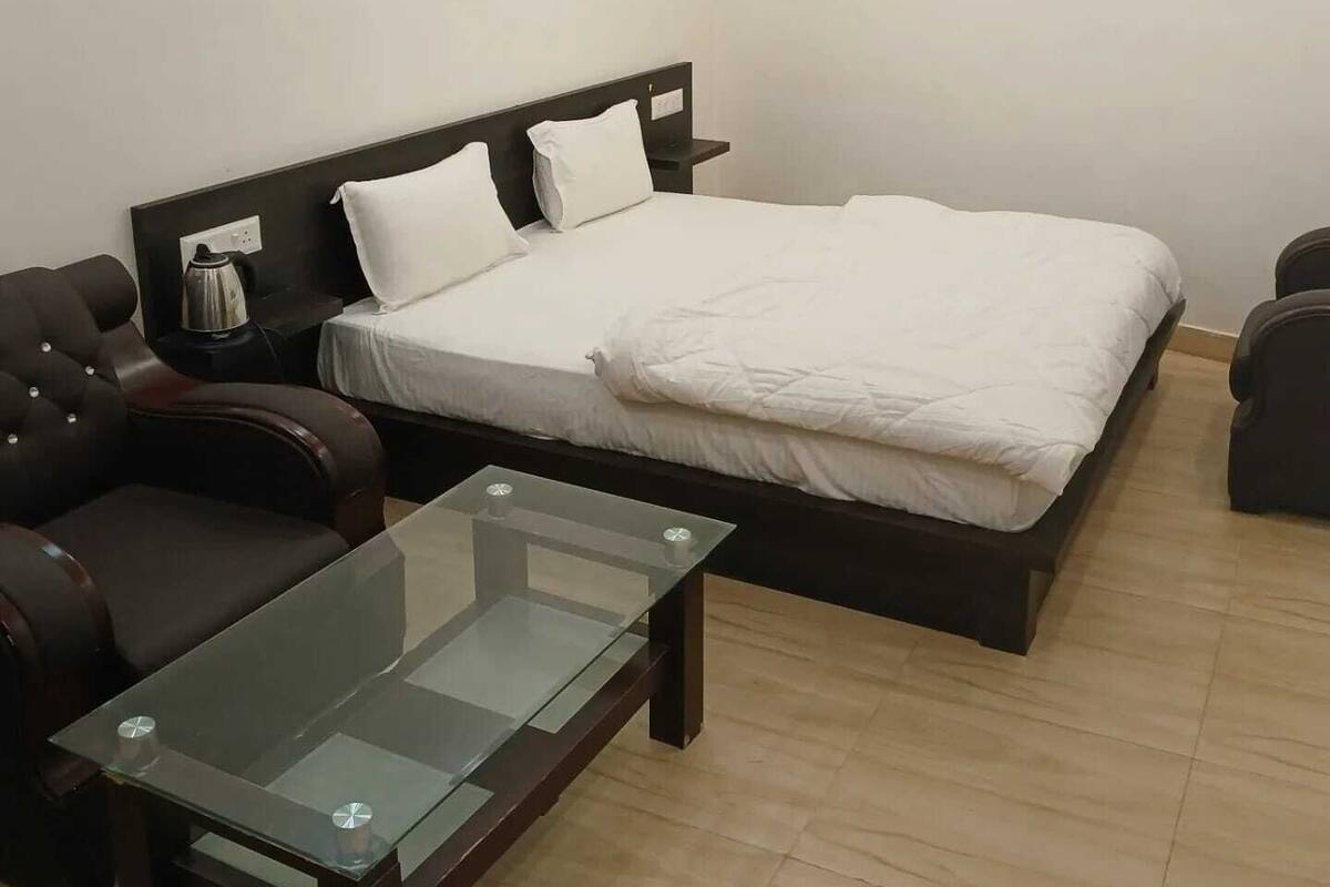 A bedroom with a bed, a glass-top table, and two leather chairs.