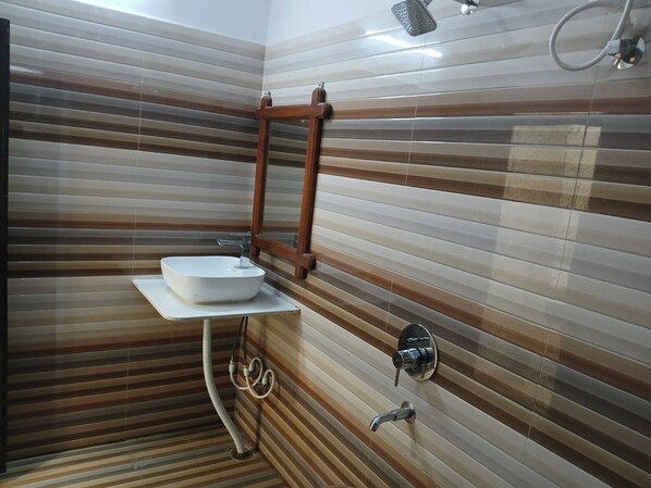 A bathroom with a wooden-framed mirror, a white sink, and a showerhead. - Avini's Garden & Hotel By GRB (Khagaria)