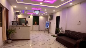 Un vestíbulo de hotel con mostrador de recepción, una araña de cristal, ventilador de techo y un sofá.