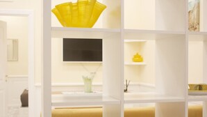 Un baño moderno con estantes blancos, un dispensador de jabón amarillo y una pantalla de televisión negra.