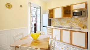 Una cocina compacta con armarios blancos, microondas y un lavamanos. Hay una mesa de comedor con sillas y un tazón amarillo.