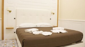 Una habitación de hotel con una cama grande, cabecera blanca y estante de madera.