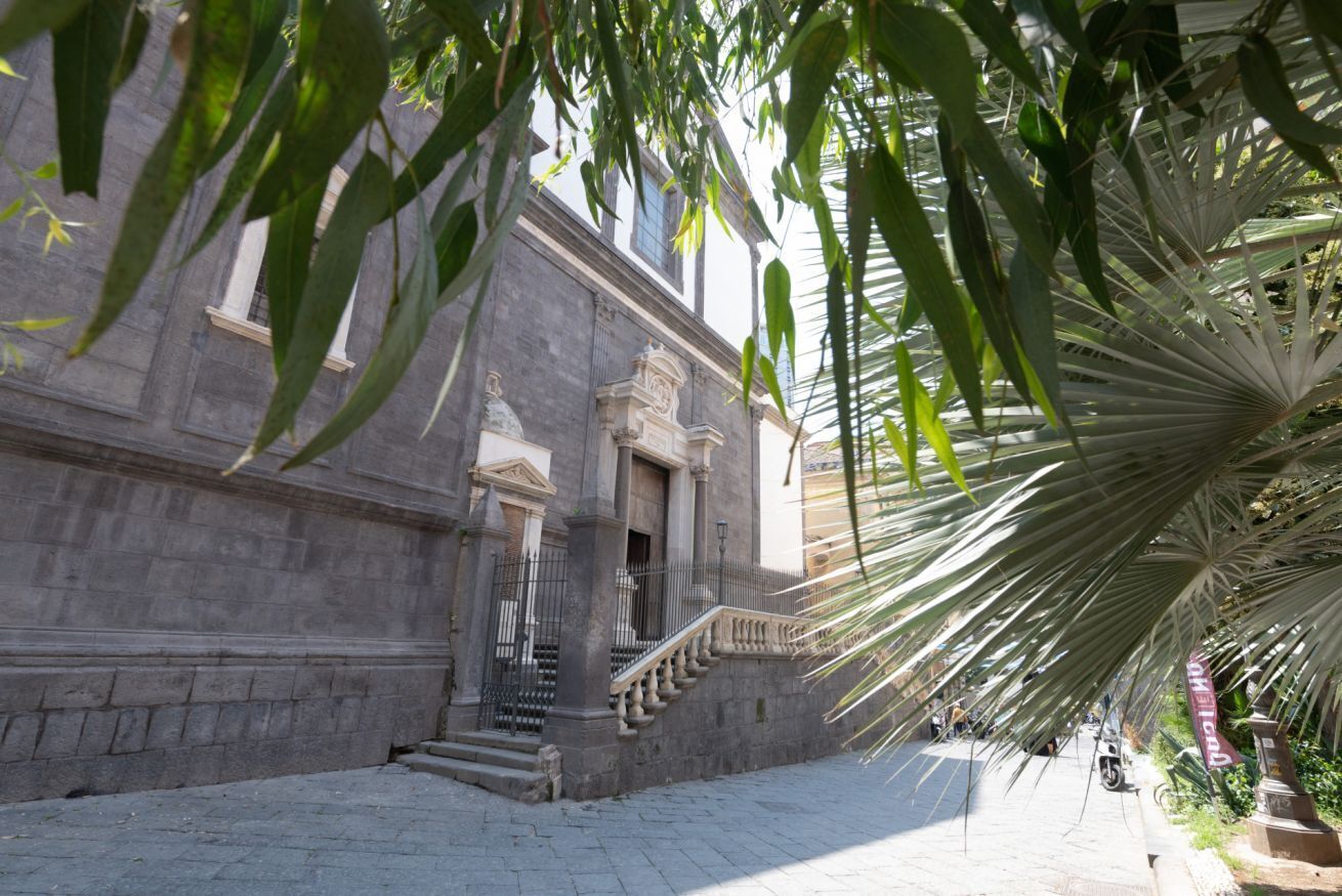 A stone building with a grand staircase leading to a door, surrounded by lush greenery.