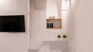 En moderne trappe med fladt design, et ophængt fjernsyn og minimalistisk indretning, herunder en lille hylde med pynteting og to plantekasser.