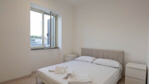 Une chambre à coucher propre et moderne, dotée d’un grand lit, de deux tables de chevet et d’une fenêtre avec des stores.