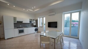 Une cuisine moderne avec des meubles blancs, un four à micro-ondes et une cuisinière. On y trouve une table à manger avec des chaises et un téléviseur fixé au mur.