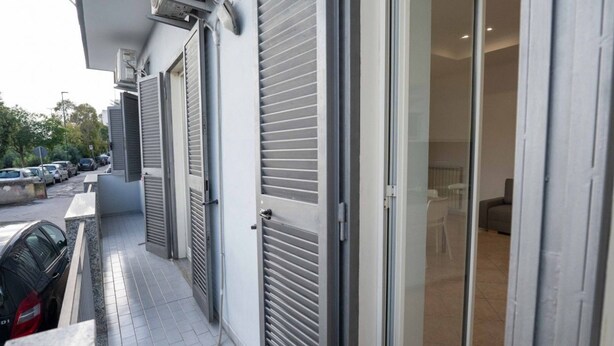 Un bâtiment moderne avec des volets fermés, un balcon carrelé et des voitures garées.