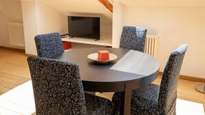 A dining area with a round table, floral-patterned chairs, a television on a shelf, and a radiator.