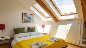 A bedroom with a skylight, a bed with a yellow bedspread, and a bedside table with a lamp.