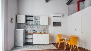 Een compacte keuken met witte kastjes, een inbouwfornuis, en een eethoek met een houten tafel en gele stoelen.