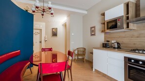 A compact kitchen with a microwave, stove, and modern cabinetry. A dining area with a red table and chairs is adjacent to the kitchen. - Da Luca e Laura by Dimorra (Napoli)