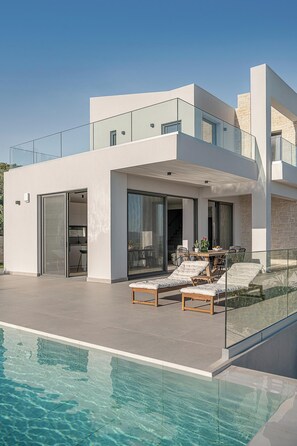 A modern house with a swimming pool, glass railings, and a patio area with outdoor furniture. - Villa Levante With Sea View (Platanias)