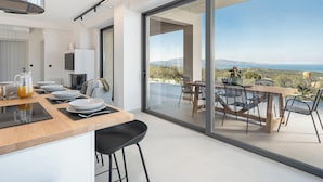 A modern kitchen with a large sliding glass door leading to an outdoor dining area with a scenic view. - Villa Levante With Sea View (Platanias)