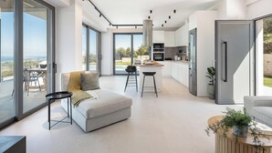 A modern kitchen with a central island, large windows, and a view of the outdoors. - Villa Levante With Sea View (Platanias)