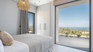 A bedroom with a large window, a bed, and a hanging light fixture. - Villa Levante With Sea View (Platanias)