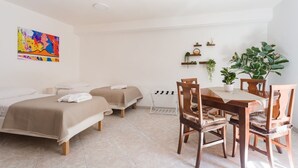 A hotel room with two beds, a dining table with chairs, a small kitchen area, and a large potted plant. - Covino House By Dimorra (Napoli)