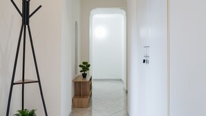 A hallway with a coat rack, a small wooden table with a plant, and a door at the end. - Covino House By Dimorra (Napoli)