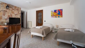 A hotel room with a stone wall, a TV, two beds, a painting, and a wooden desk. - Covino House By Dimorra (Napoli)