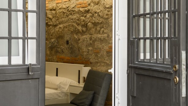 A room with a bed, a chair, and a stone wall. - Dimora al Cristo Velato By Dimorra (Napoli)