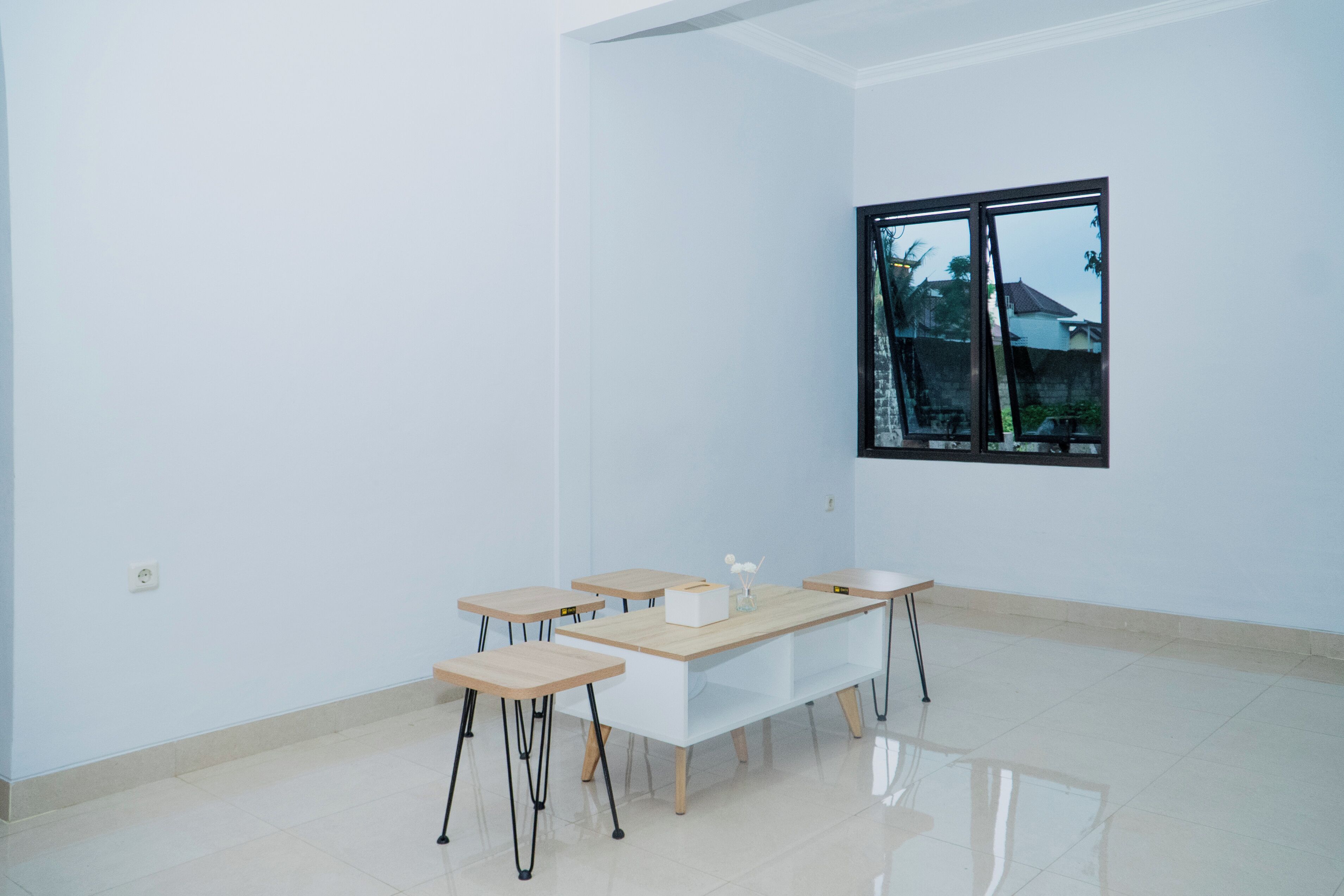 A spacious room with a large window, a long table with four chairs, and a white wall.