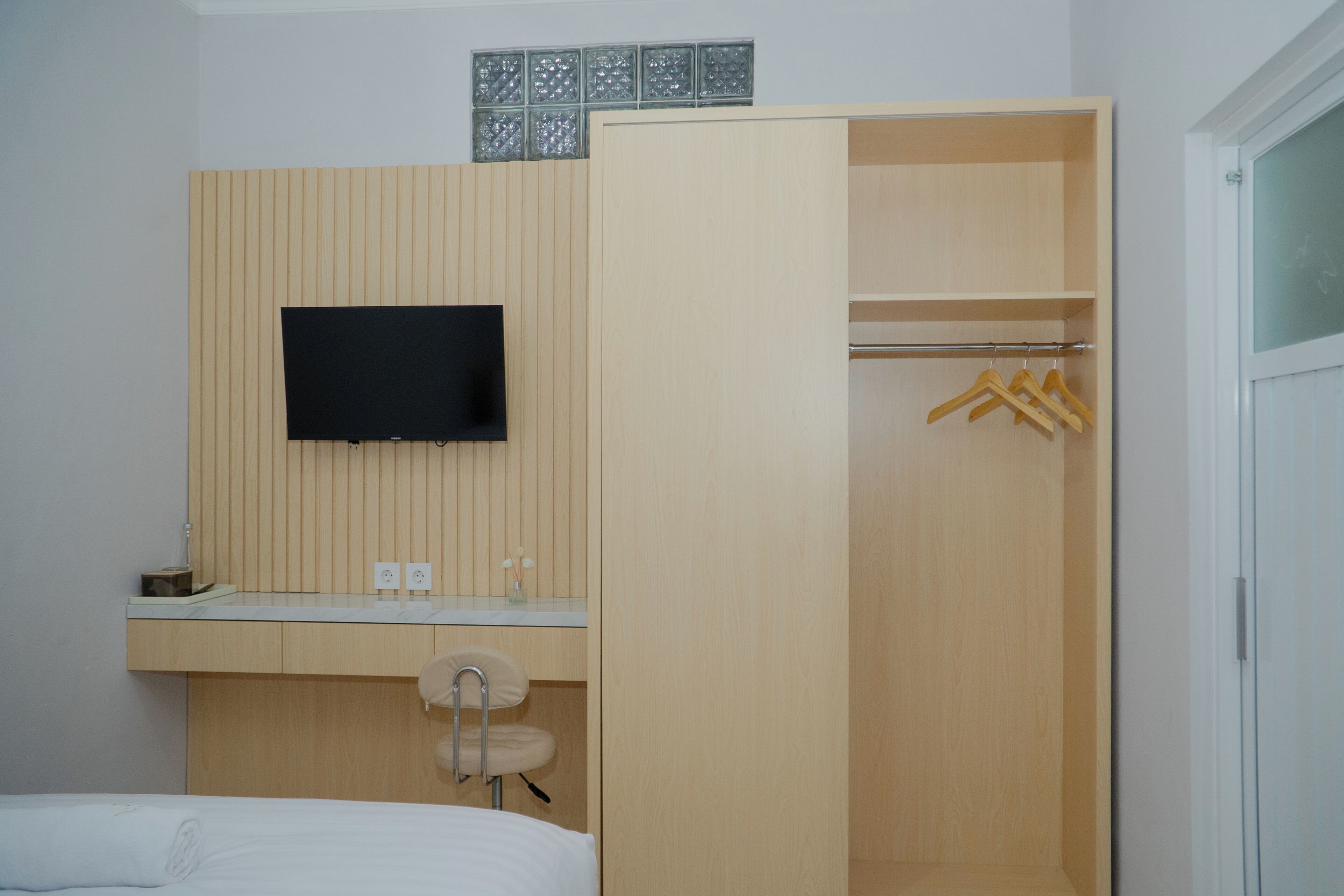 Een slaapkamer met een bed, een aan de muur bevestigde televisie, een houten garderobe en een badkamer met wastafel en spiegel.