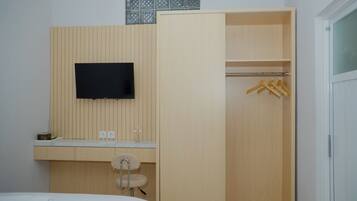 Een slaapkamer met een bed, een aan de muur bevestigde televisie, een houten garderobe en een badkamer met wastafel en spiegel.