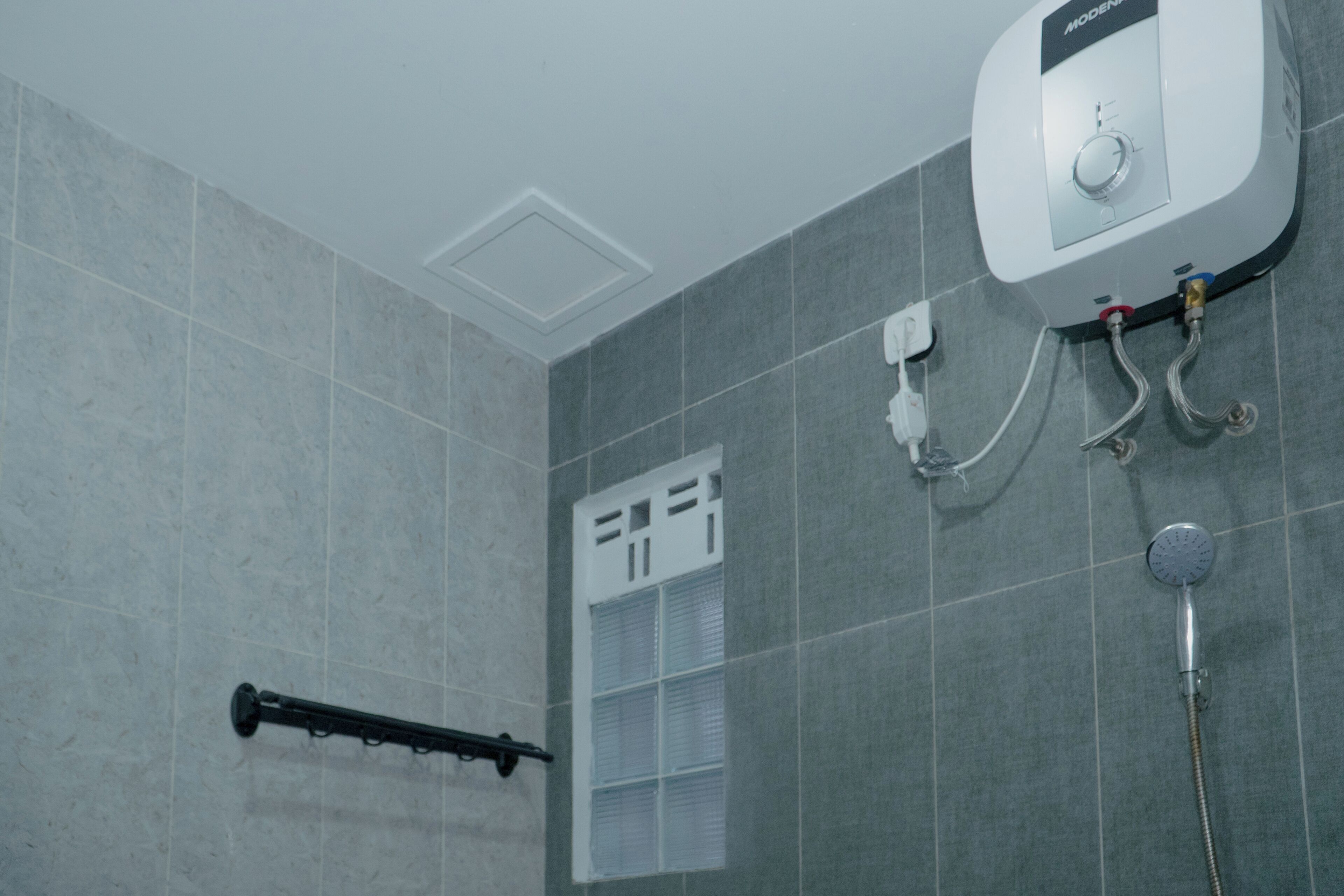 Bagno con piastrelle grigie, soffione doccia, doccetta manuale e scaldasalviette a parete.