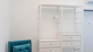 A white closet with multiple shelves and drawers, a hanging rod, and a teal chair.