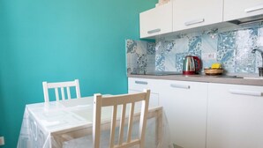 A small kitchen with white cabinets, a tiled backsplash, and a table with chairs.