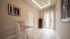 A spacious room with a wooden floor, a white chair, a small table, a door, and a window with curtains.