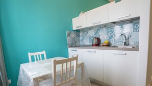 A small kitchen with white cabinets, a tiled backsplash, and a table with chairs.