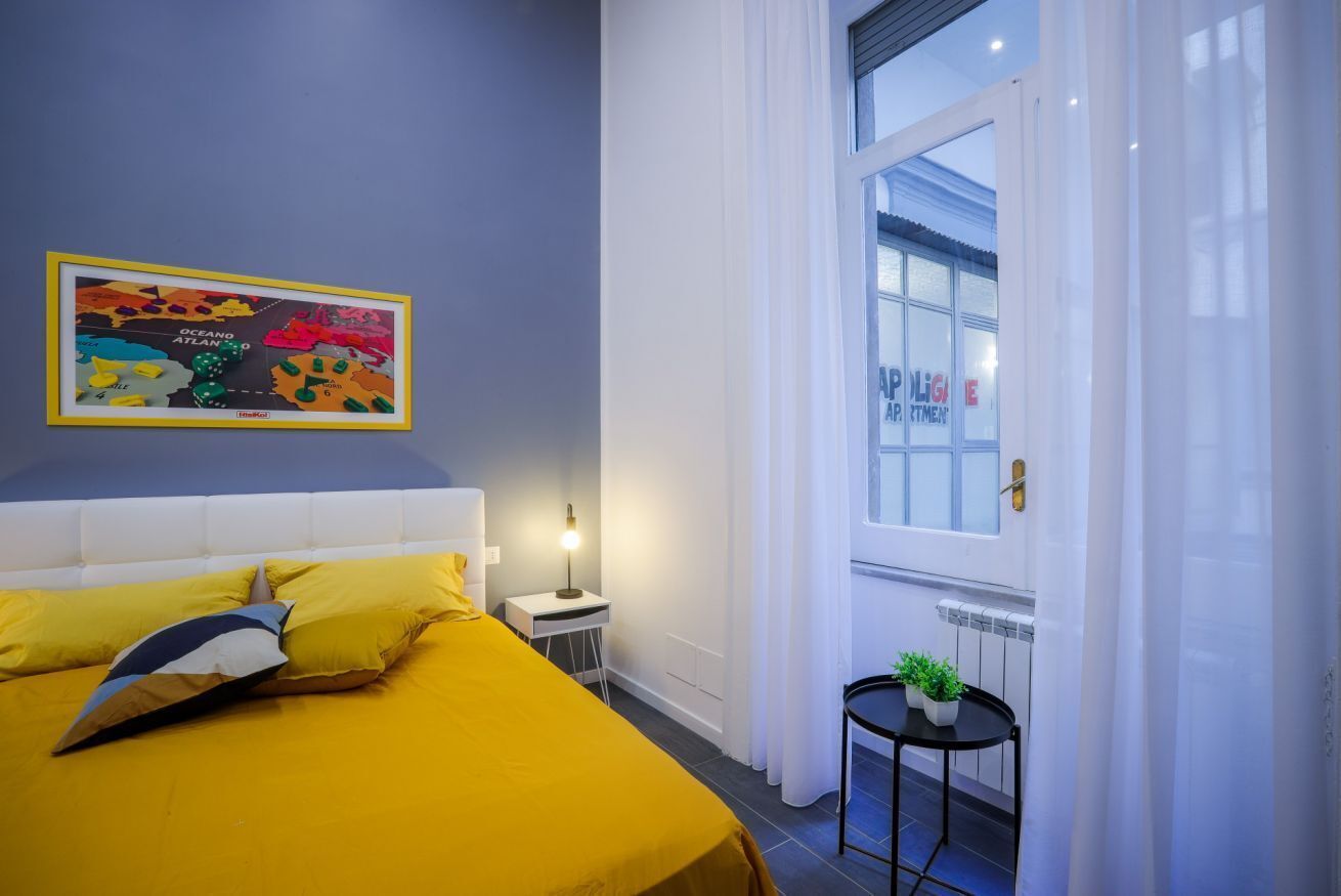 Een kamer met een bed, een tafeltje met planten, een raam met gordijnen en een kleurrijke kaart aan de muur.