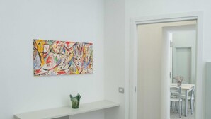 A modern interior with a white wall, a colorful abstract painting, and a small green vase on a white shelf. - New Corte 2 By Dimorra (Napoli)