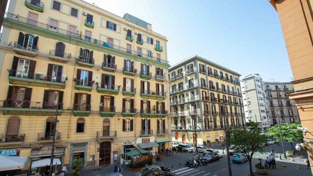 A street view of a multi-story building with balconies, shops on the ground floor, and cars parked along the street. - New Corte 2 By Dimorra (Napoli)