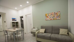 En moderne stue med en grå sofa, et spisebord med stole, og et farverigt abstrakt billede på væggen.