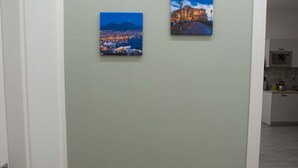 A hallway with two paintings on the wall, a door on the left, and a glimpse of a kitchen area in the background.