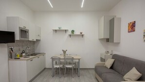 A modern kitchen with a dining area, a grey sofa, and a flat-screen TV mounted above the counter.