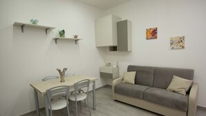 Una sala de estar moderna con un sofá gris, una mesa de comedor con sillas y una pequeña cocina con un microondas.