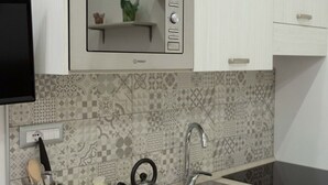 Una cocina con baldosas estampadas, microondas, tetera y lavabo.