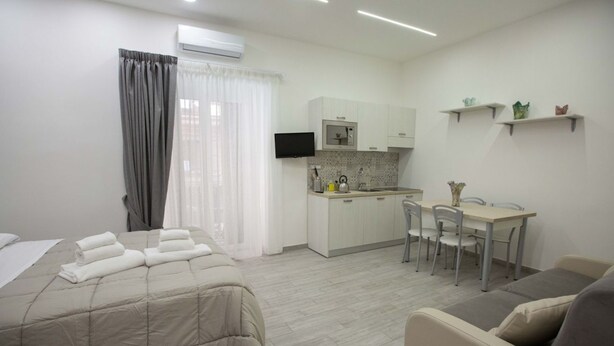 Habitación de hotel compacta con cama, kitchenette pequeña, zona de comedor y televisor.