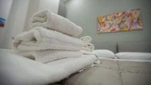 Un montón de toallas blancas ordenadas sobre una cama en una habitación de hotel, con un cuadro abstracto de colores en la pared.