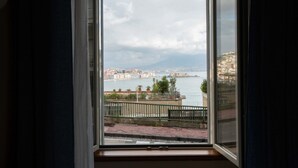 Vista desde una ventana a una ciudad costera, con edificios, una masa de agua y una montaña distante.