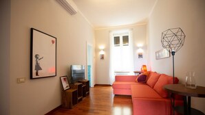 Una sala de estar con piso de madera, un sofá rosa, un televisor y un cuadro en la pared.
