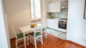 Una pequeña cocina con armarios blancos, salpicadero de azulejos y zona de comedor con mesa y sillas.