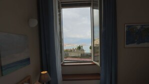 Habitación de hotel con cama, lámpara de noche, ventana y vistas a la ciudad y al agua.