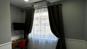 A hotel room with a bed, a desk with a chair, a TV mounted on the wall, and a window with curtains. - Dimorra Boutique room 2 (Napoli)