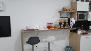 A small kitchenette with a microwave, toaster, and various food items on the counter. There are two chairs and a trash bin. - Dimorra Boutique room 2 (Napoli)